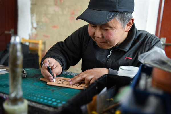        4月15日，在锡尼河镇的出租房内，米格木尔在皮制品上雕刻花纹。米格木尔家住内蒙古鄂温克族自治旗锡尼河镇孟根础鲁嘎查。年轻时因为一场意外，他的腿脚落下病症。2016年，因为缺失劳动能力，他成了建档立卡贫困户。 2016年下半年，女儿南吉乐玛需要到镇上的蒙古族幼儿园上学。为了孩子的学习，独自抚养女儿的米格木尔选择离开牧区来到镇上租房陪读。因为腿疾不便打工，租房生活支出也大，虽然看病不用花钱，但米格木尔的生活压力还是不小。 正当米格木尔犯难之际，2018年春天，当地就业部门推荐他去民族文化产业创业园参加皮雕手艺培训。米格木尔十分珍惜这次培训机会，坚持学习三个月后，他便能独自在家做产品，并达到公司售卖标准。这个手艺让他居家赚钱、陪读两不误，逐步实现稳定脱贫。 在鄂温克族自治旗，通过民族文化产业创业园培训手工艺技能成为当地扶贫的一大特色。在园区内，民族特色企业达到了192家，囊括23项非遗传承项目。至今，创业园已为全旗近300户建档立卡贫困户开展特色产业培训。 新华社记者 刘磊 摄