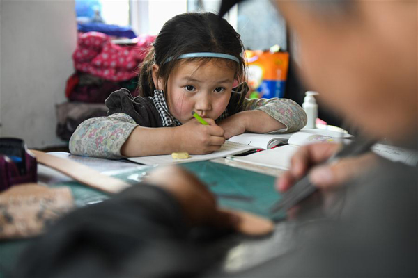        4月15日，在锡尼河镇的出租房内，女儿南吉乐玛写作业时看爸爸制作皮制品。新华社记者 刘磊 摄
