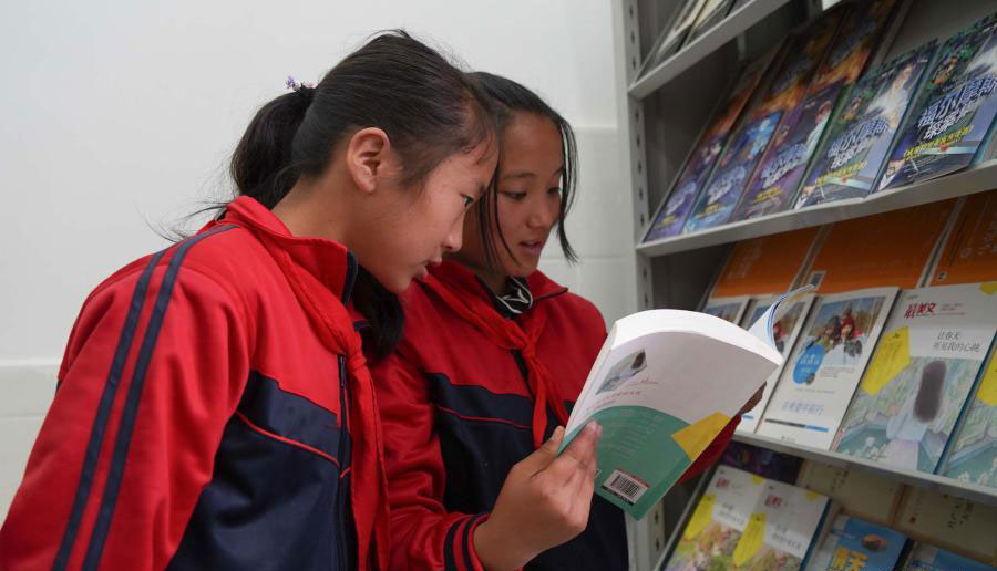 在四川省布拖县阿布泽鲁小学，海莫惹牛（右）和同学在新建的图书馆里阅读新书（6月23日摄）。